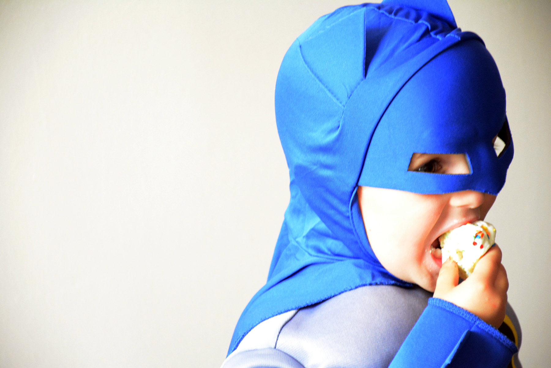 young boy in Batman costume eating a cupcake