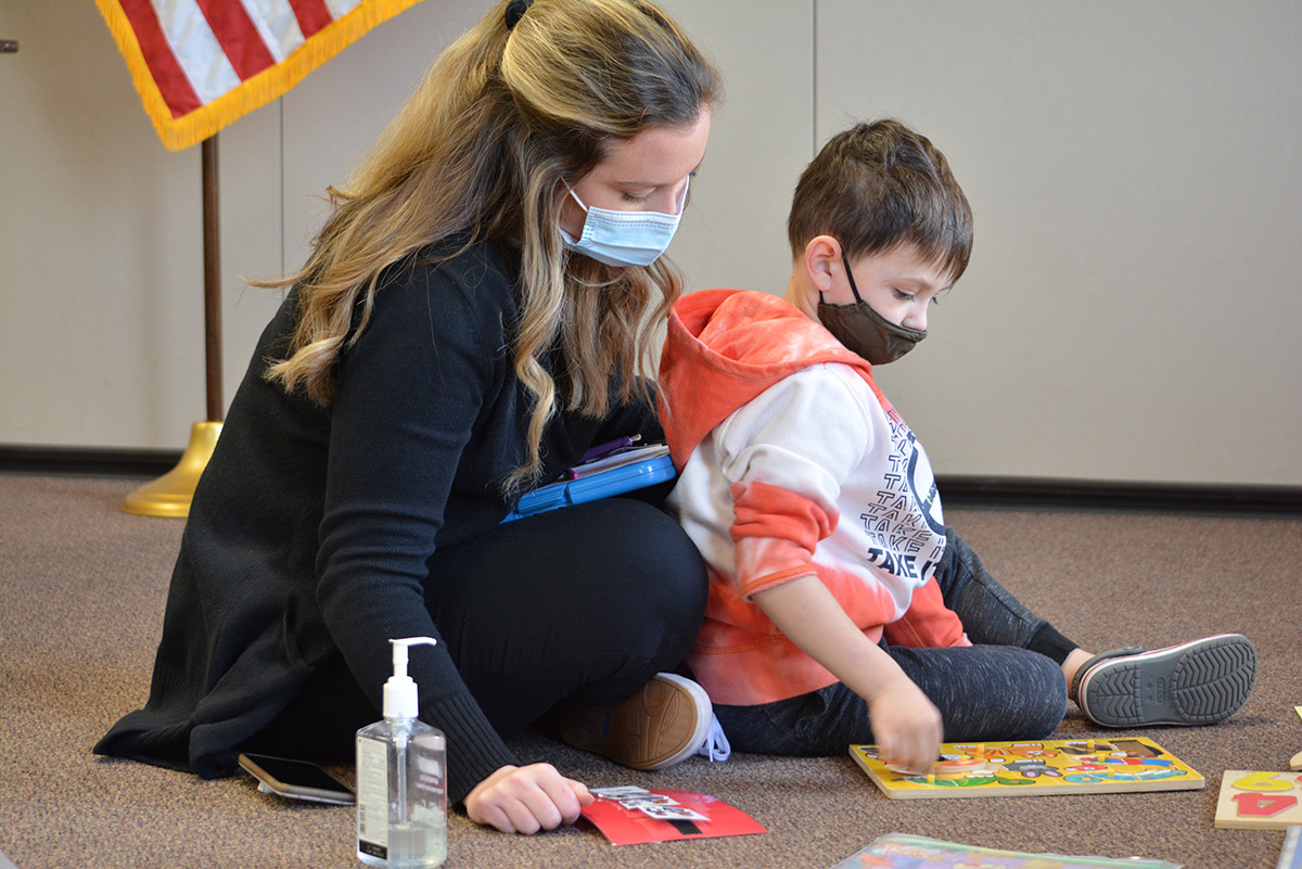 A lady and a boy doing a puzzle with masks on.