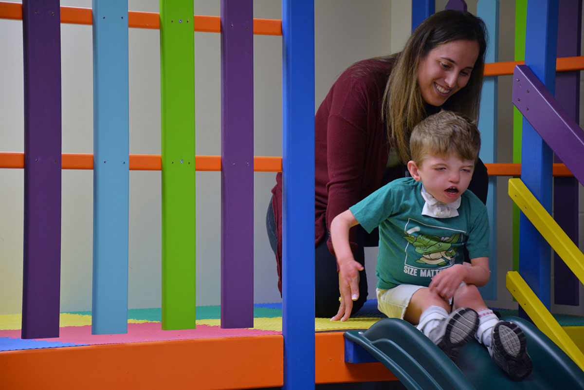 A lady helping a boy down a slide.