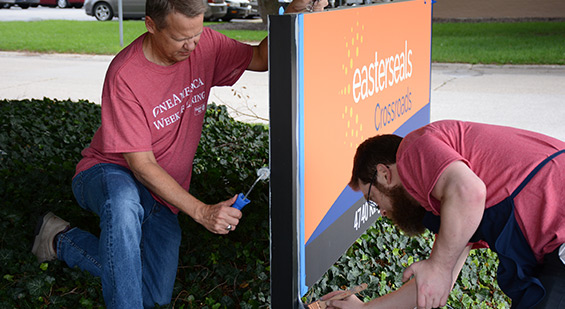 Two volunteers painting an Easterseals Crossroads sign.