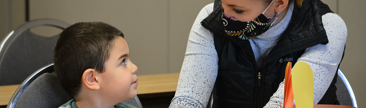 Lady wearing mask teaching a young boy.